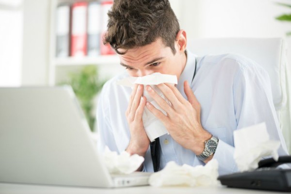 Young business man blows his nose while working at his laptop in the office. Young business man blows his nose while working at his laptop in the office.